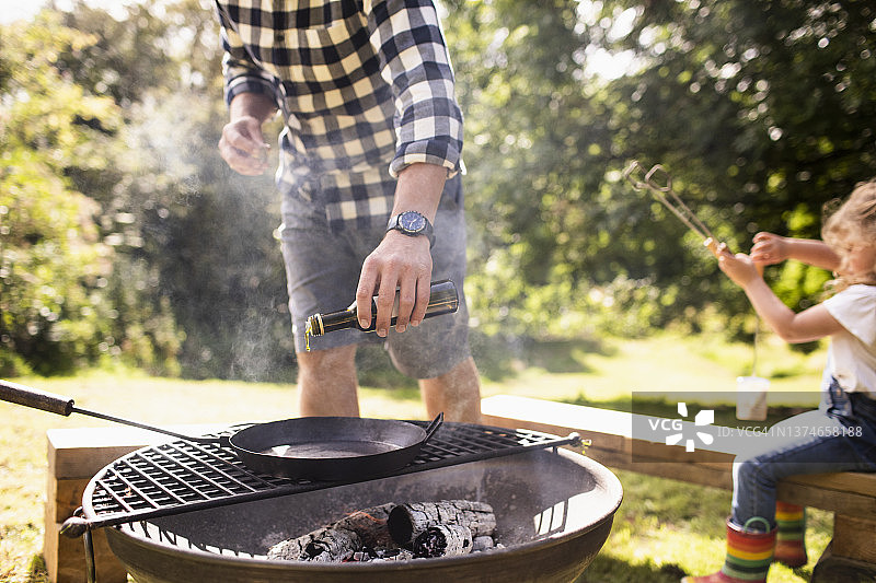 男子在后院烧烤架上的铸铁煎锅上倒橄榄油图片素材
