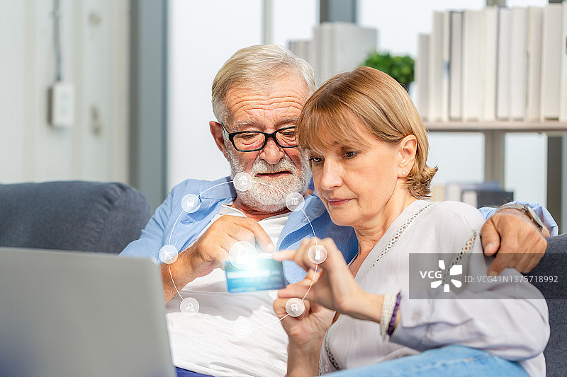 老年夫妇在客厅网上购物，老年男女在舒适的沙发上使用电脑笔记本电脑，幸福的家庭概念图片素材