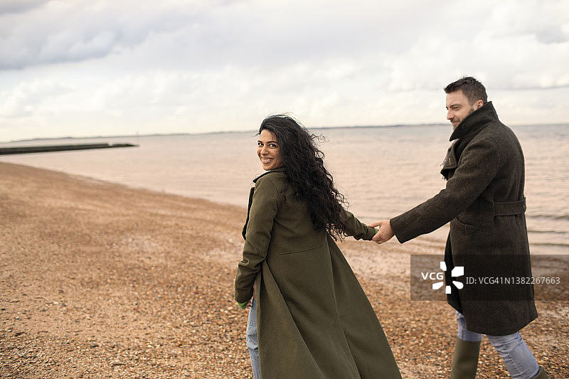 穿着冬衣的幸福情侣在海滩上手牵着手图片素材
