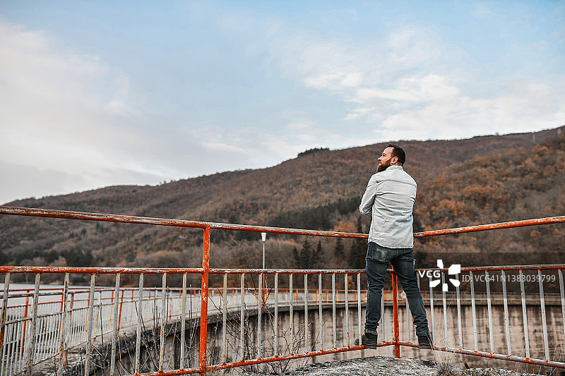 男人站在水坝栏杆上，为人类更美好的未来而感到成就感图片素材
