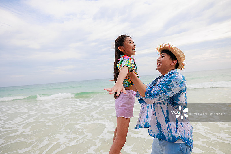 一位亚裔父亲在沙滩上抱起女儿。旅游、家庭、休闲的理念图片素材