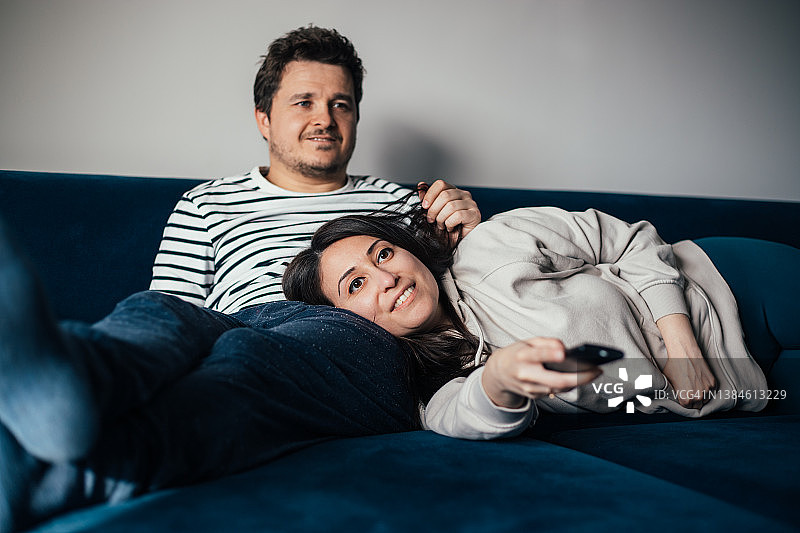 女人躺在他男朋友的腿上，和他一起在沙发上看电视图片素材