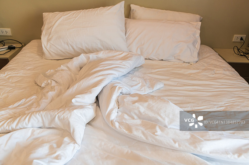公寓酒店卧室里凌乱的床上有被子和枕头图片素材