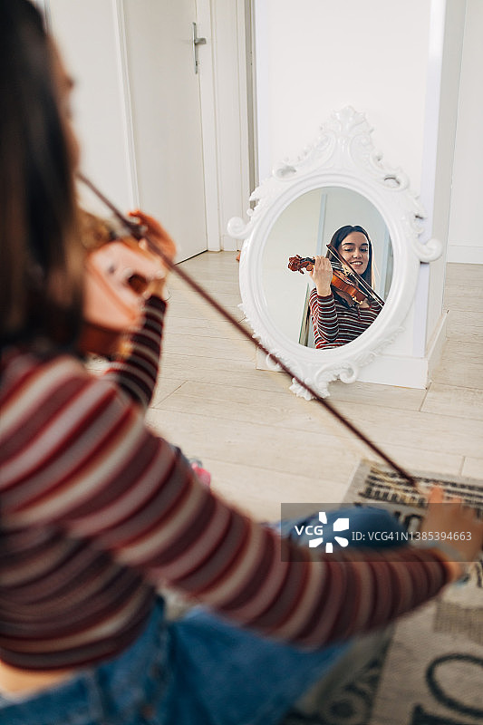 年轻女小提琴手练习拉小提琴时镜中的影像。图片素材