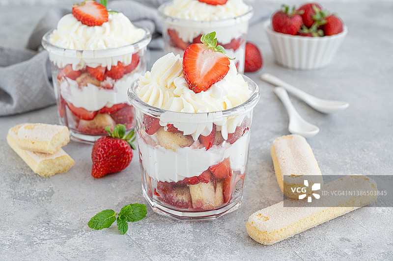 草莓提拉米苏或松糕，在一个玻璃罐里的甜点，新鲜的草莓和薄荷叶在灰色的背景上图片素材