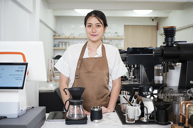 小型企业咖啡厅特许经营解决方案。一名亚洲女性咖啡馆老板在咖啡馆柜台微笑的肖像。她利用技术提高客户服务和满意度。图片素材