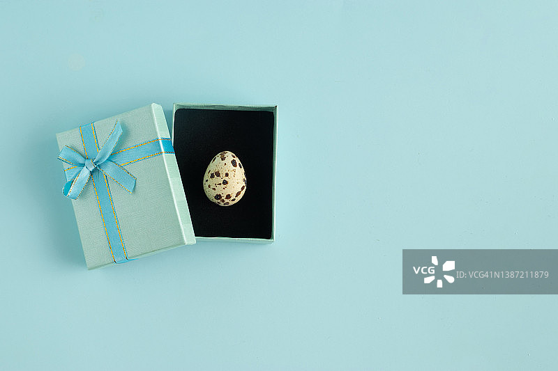 在浅蓝色的背景下，蓝色的礼品盒里有一个小小的复活节彩蛋。创意假期或美食概念图片素材