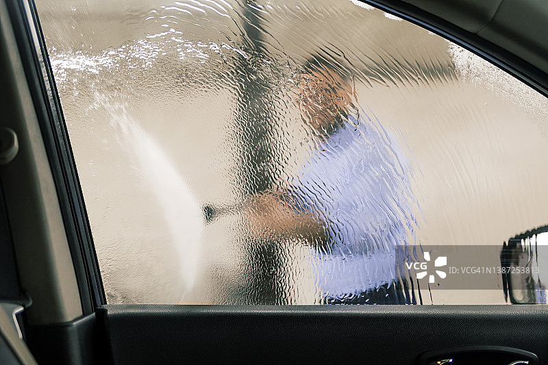 一名男子用水管清洗车窗，这张照片是从车内拍摄的图片素材