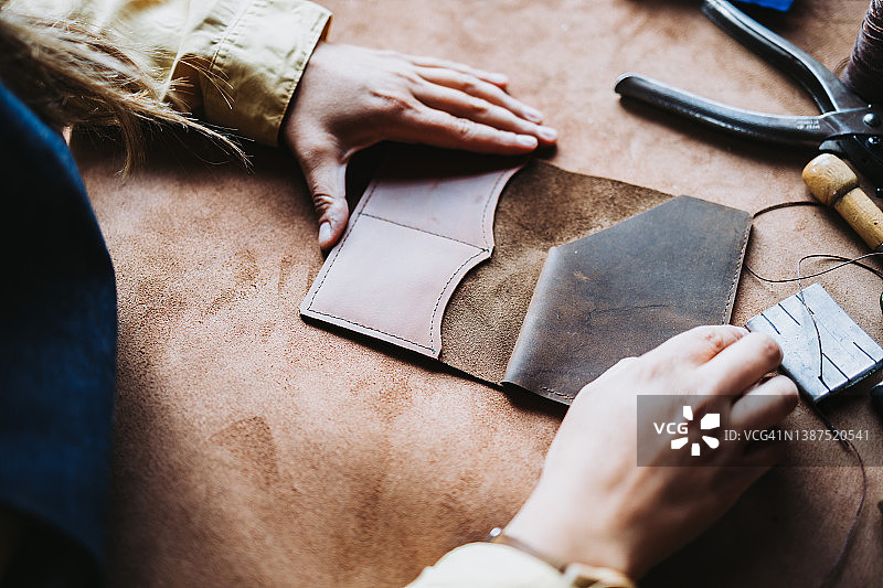 一个不知名的女人在她的设计工作室和工作空间完成一个皮革钱包。皮革女手艺人。独立的小型企业。工人的一天。Marroquineria。图片素材
