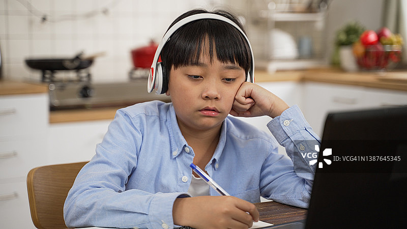 疲惫的亚洲青少年睡在桌子前的笔记本电脑在家里。筋疲力尽的青少年学生在网上学习时感到困倦。图片素材