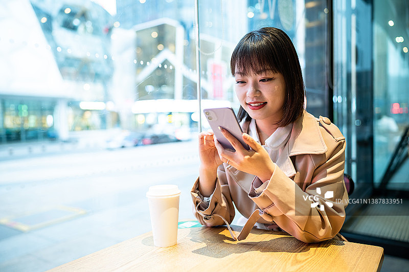 亚洲年轻女性在咖啡店使用智能手机图片素材