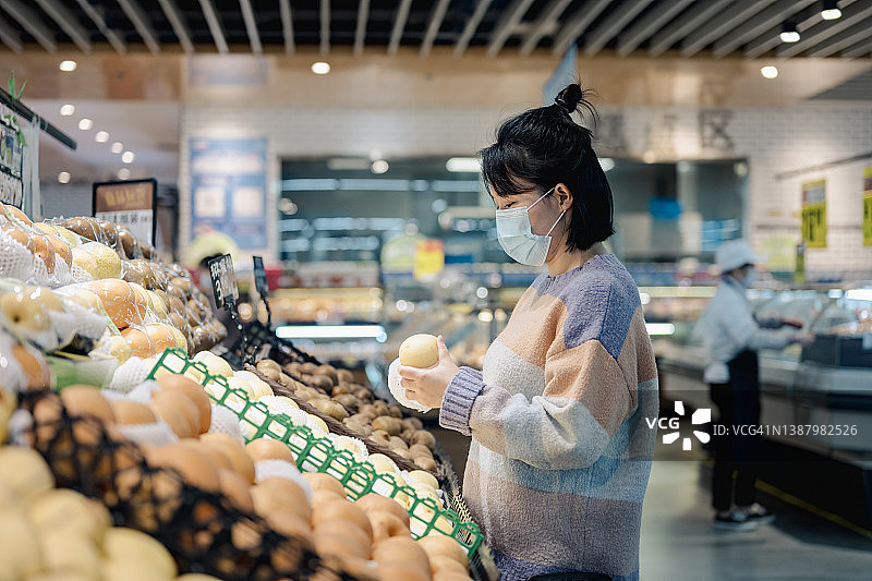 一个戴着医用口罩的年轻女子在水果摊前买梨图片素材
