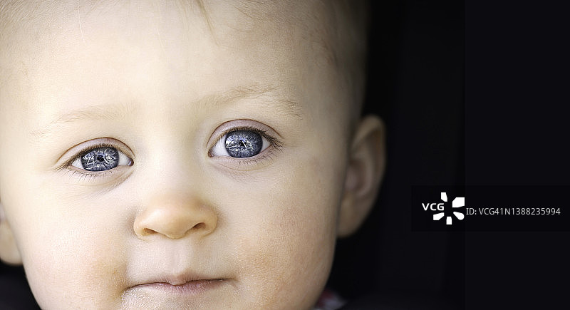 可爱的15个月大的女婴直视着镜头，眼睛清澈湛蓝，脸上带着自然温柔的微笑。图片素材