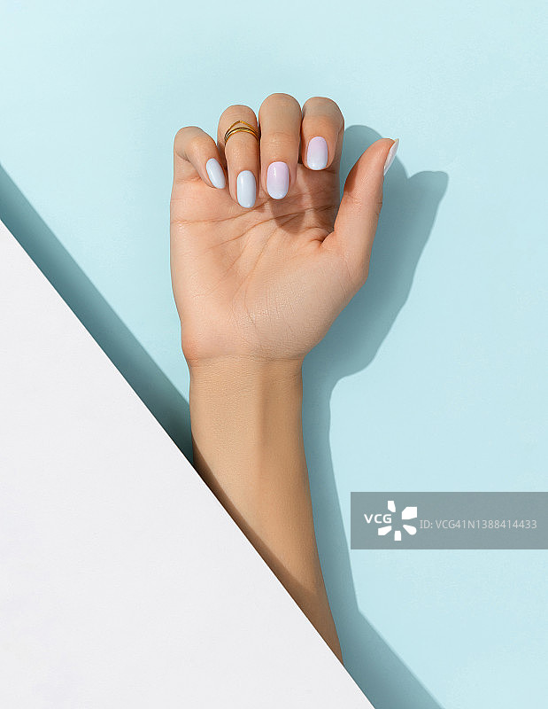女人的手与时尚的指甲在蓝色的背景。夏天钉设计图片素材