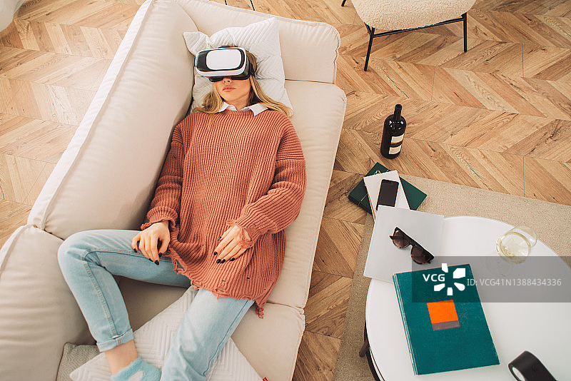戴着虚拟现实眼镜的可爱女人坐在家里的沙发上图片素材