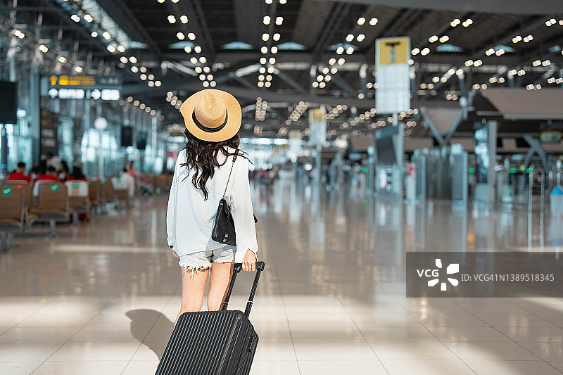 年轻的亚洲女性带着护照，提着手提箱在机场大厅走动图片素材