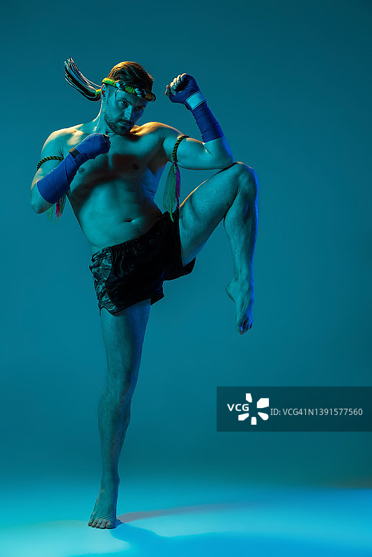 膝盖踢。动态肖像的专业泰拳练习孤立在蓝色的工作室背景。体育，泰拳，比赛，搏击俱乐部的概念图片素材