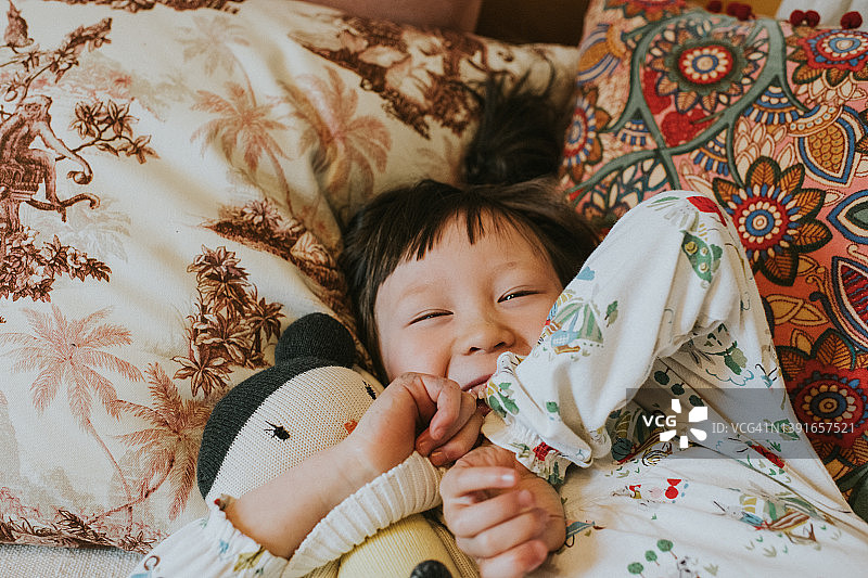 一个可爱的小女孩在床上微笑的特写，抱着她的洋娃娃图片素材