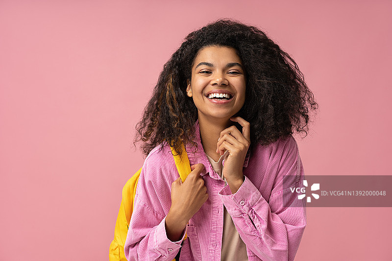 微笑的非洲裔美国学生拿着背包看着相机孤立在粉红色的背景。教育的概念图片素材