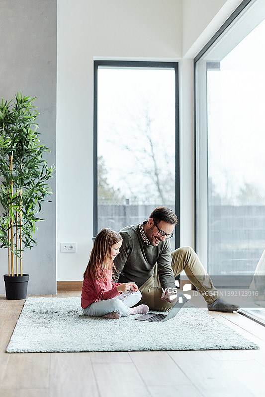 快乐的单身父亲和他的女儿在家里使用电脑。图片素材