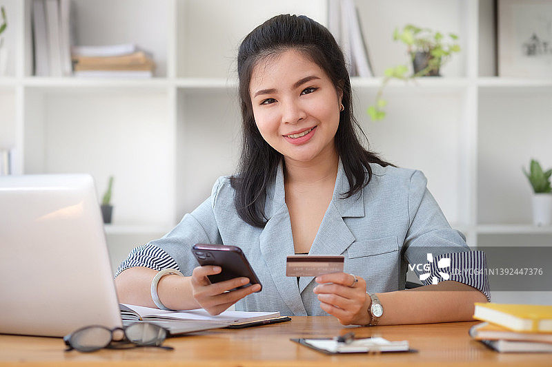 开朗的年轻亚洲女性持有信用卡和智能手机在网上购物。图片素材