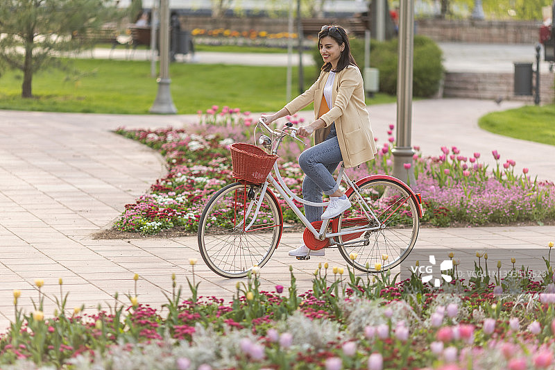 微笑的年轻女子骑着复古自行车在春天的公园图片素材