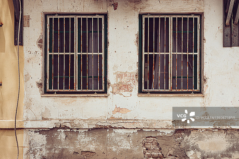 老旧破旧的建筑，白墙风化，两扇窗户上有安全栅栏图片素材