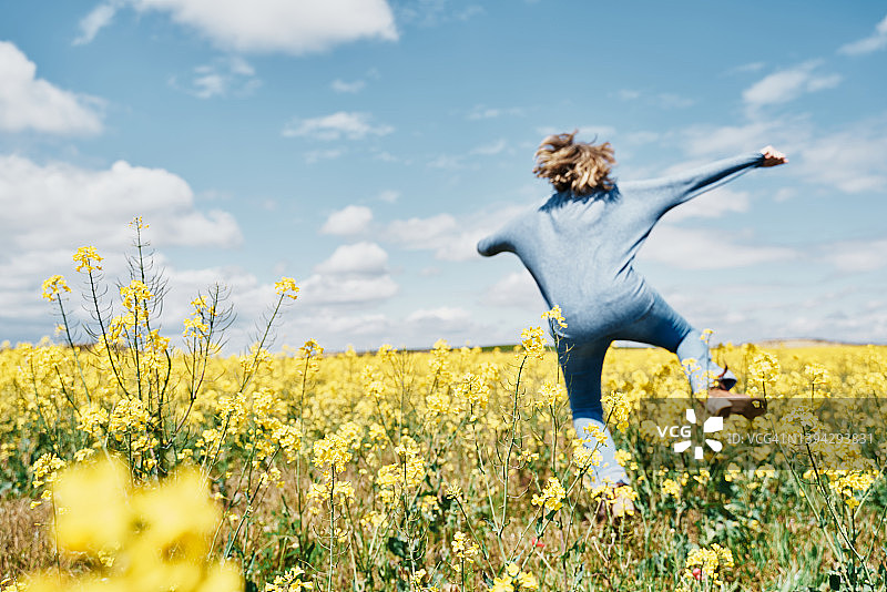天空背景下，热情的年轻女子在油菜田里跳跃图片素材