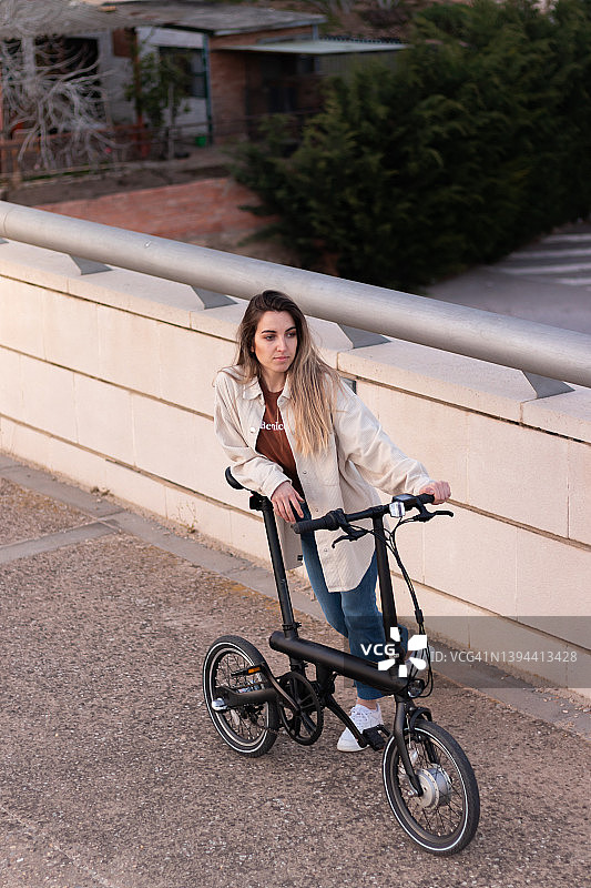 俯视图的年轻女子倾斜和持有一辆电动自行车使用替代能源，以提高能源效率图片素材