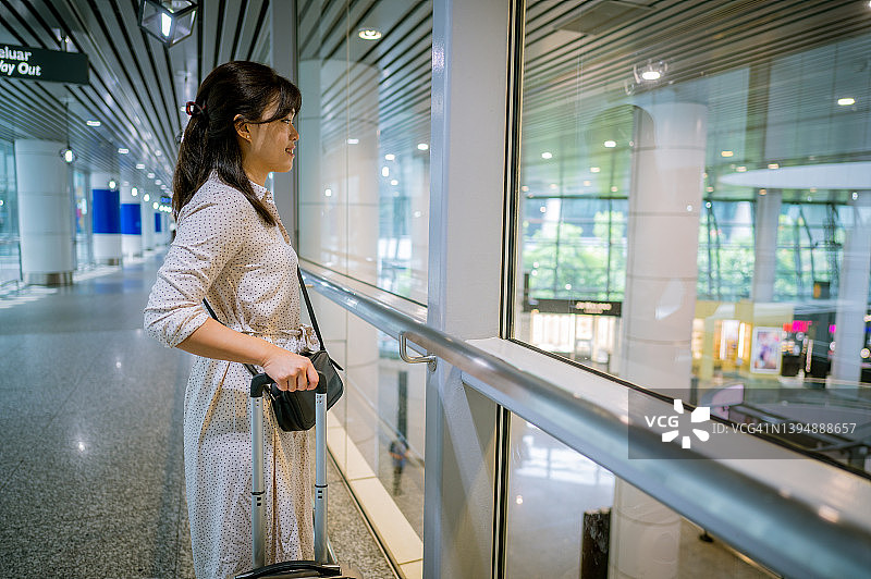 一名年轻的亚洲女子在机场候机楼拉着行李箱图片素材