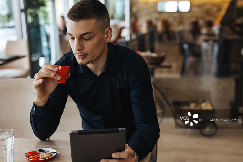 英俊的年轻人在餐厅喝咖啡，用电子平板电脑图片素材