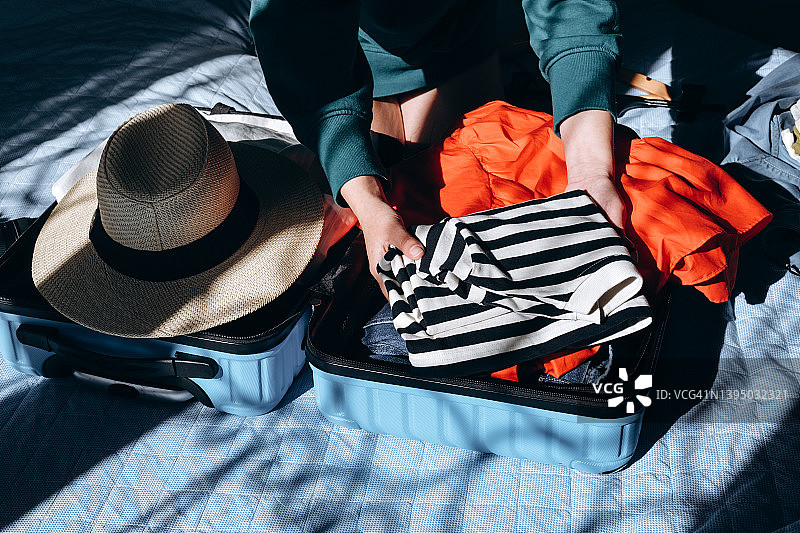 夏天的衣服放在旅行箱里，旅行箱的阴影叠加。法式条纹t恤配草帽。图片素材