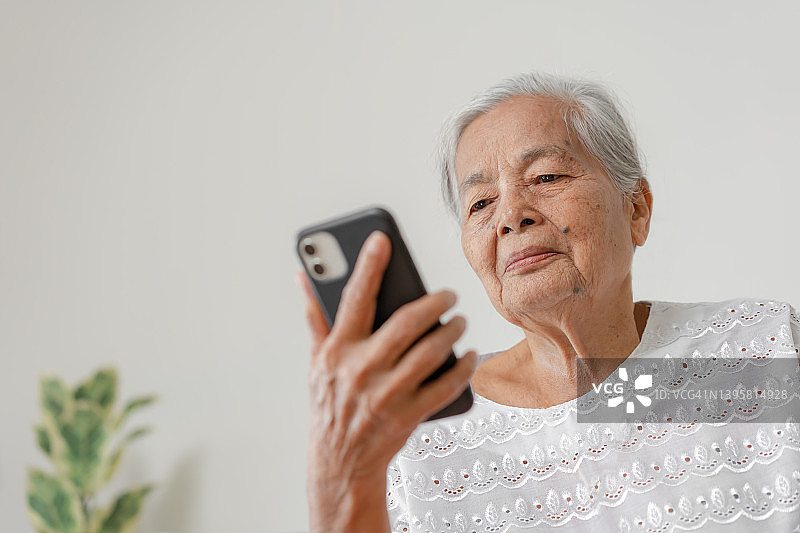 快乐的亚洲老年妇女打电话在家的智能手机。图片素材