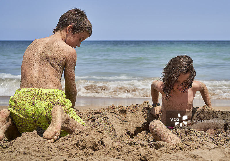 哥哥姐姐喜欢坐在阳光明媚的沙滩上玩沙子图片素材