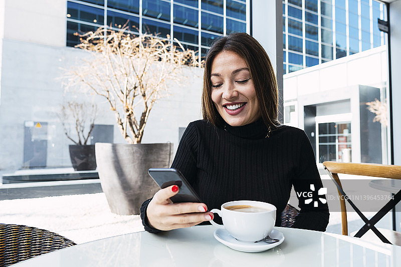 微笑的商人与咖啡杯使用智能手机坐在咖啡馆图片素材