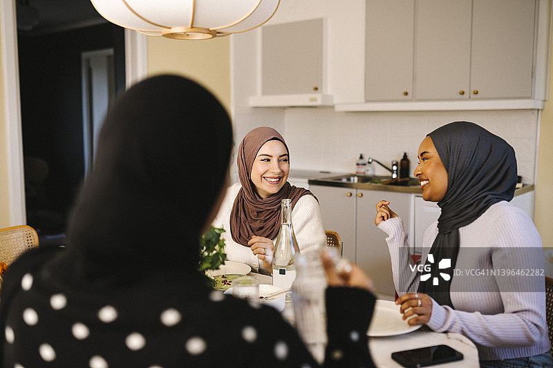 快乐的年轻女性戴着头巾在家里共进晚餐图片素材