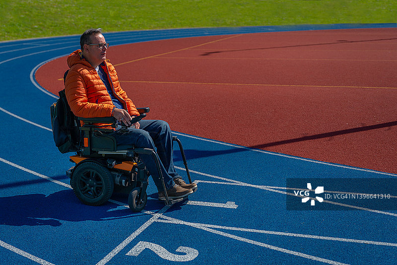 一个残疾人坐在电动轮椅上怀旧地坐在运动场上的蓝色跑步机上。图片素材