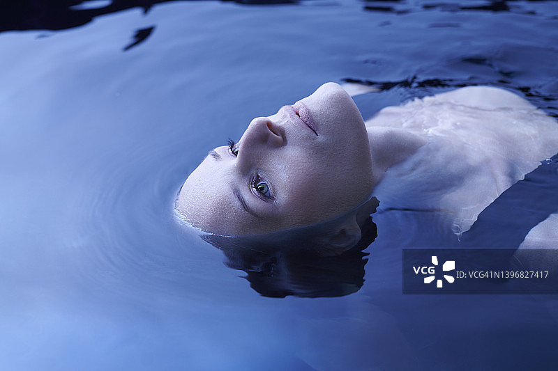 优雅的女人从清澈的蓝色海水中浮现。自然美容护理隐喻图片素材