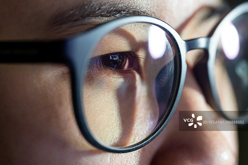 特写镜头的女人眼睛在眼镜反射一个工作的电脑蓝屏图片素材