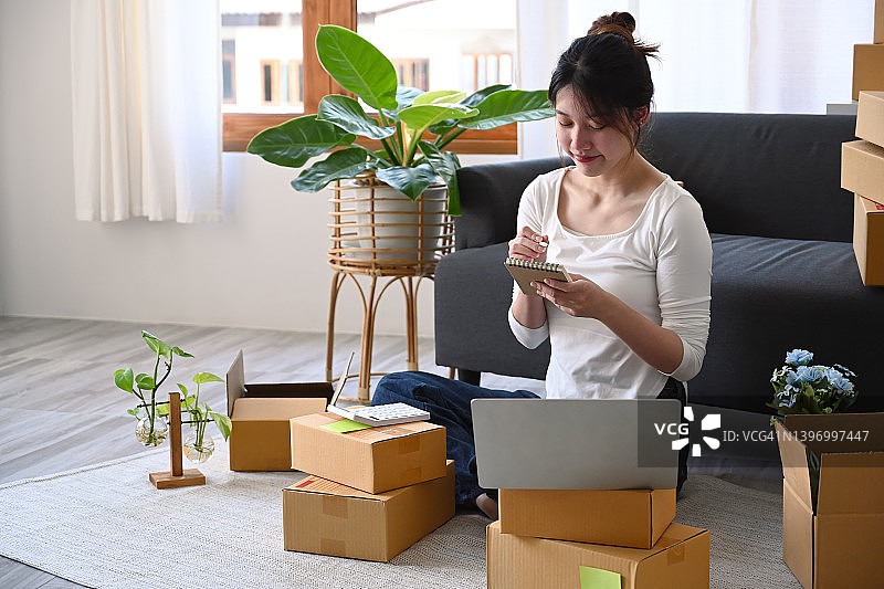 年轻的女性创业企业家在互联网上检查订单，准备产品的包裹盒交付。图片素材