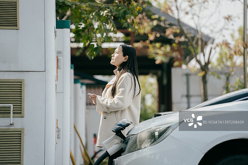 亚洲妇女正在城市公园为她的电动汽车充电图片素材