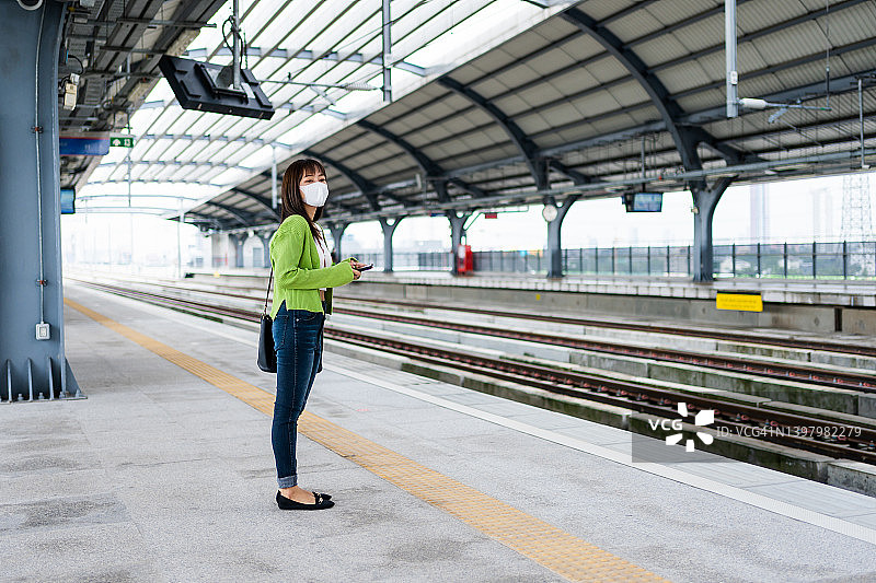 一名年轻的亚洲女性在站台上等车时正在看智能手机。图片素材