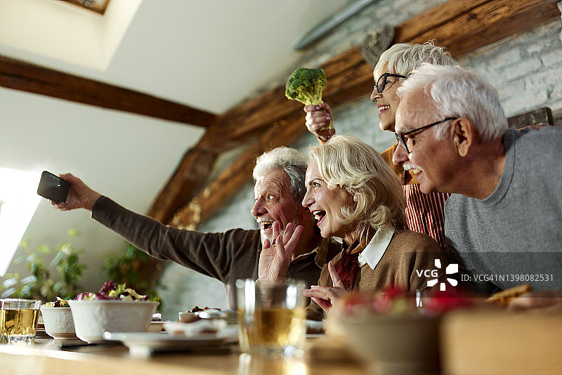 快乐的老年人在家吃饭时自拍。图片素材