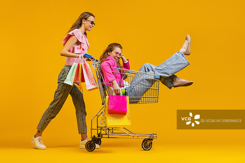 动态肖像酷年轻兴奋的女孩去购物与购物车孤立在明亮的黄色背景。销售概念，黑色星期五，折扣，情绪图片素材