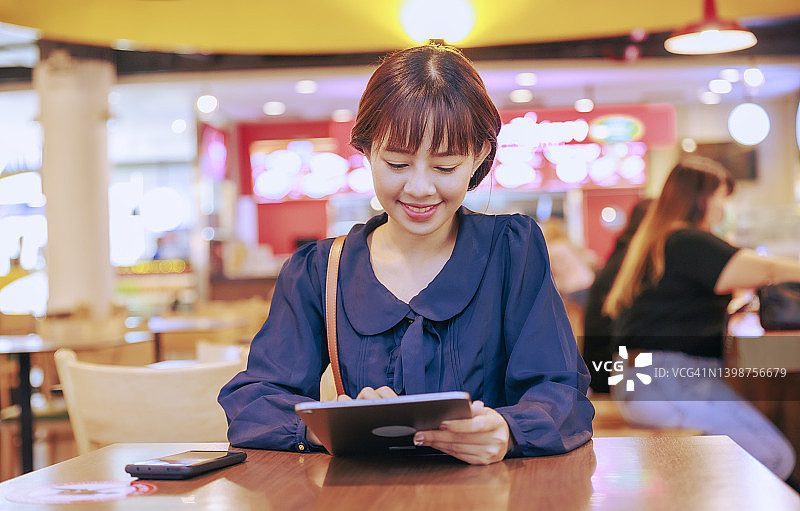 年轻的亚洲女商人在机场离境区工作或用数字平板电脑阅读电子邮件。商务旅行的概念。图片素材