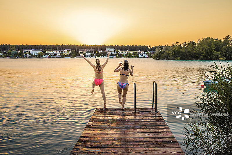 两个女性朋友在日落时跳入湖中图片素材