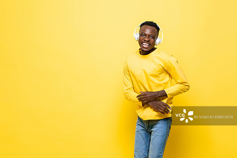 积极快乐的非洲人听音乐耳机在黄色工作室孤立的背景与拷贝空间图片素材