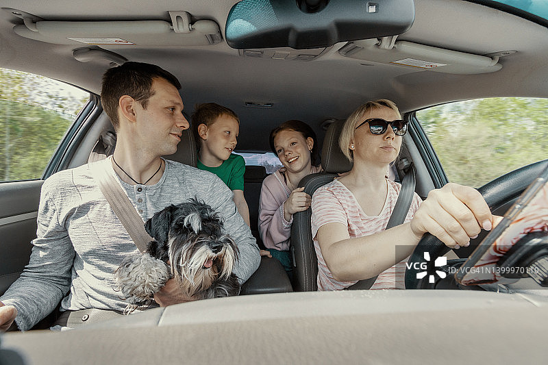 Inside view的两个父母，女儿和儿子与狗在公路旅行。女司机，正面图片素材