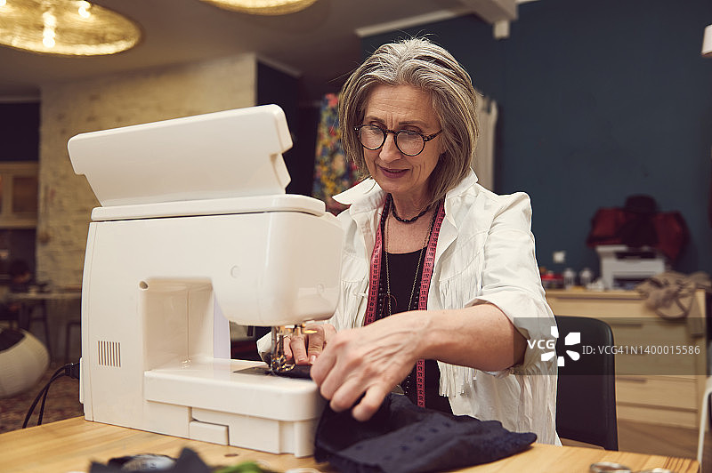 时尚时尚的服装设计师成熟的女裁缝在缝纫机上缝制。制造商、裁缝在创新发展的过程中图片素材