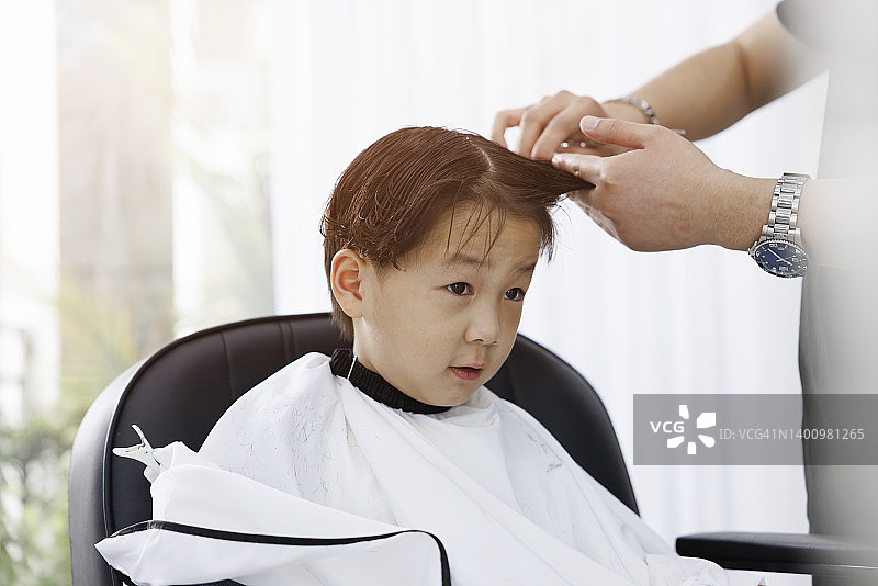 特写男人的手梳理小男孩的头发在理发店。图片素材